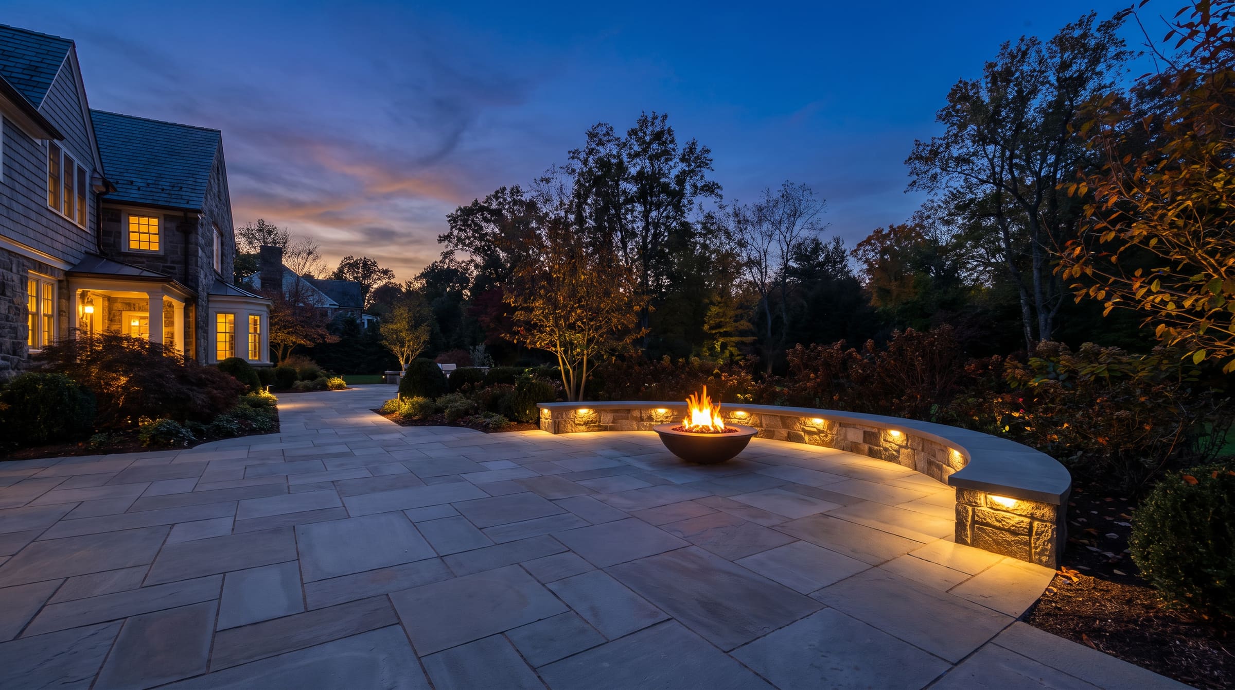 2,400 SF terrace, 62 LF seat wall, gas fire bowl in Saddle River at dusk — stand-in art at final crop